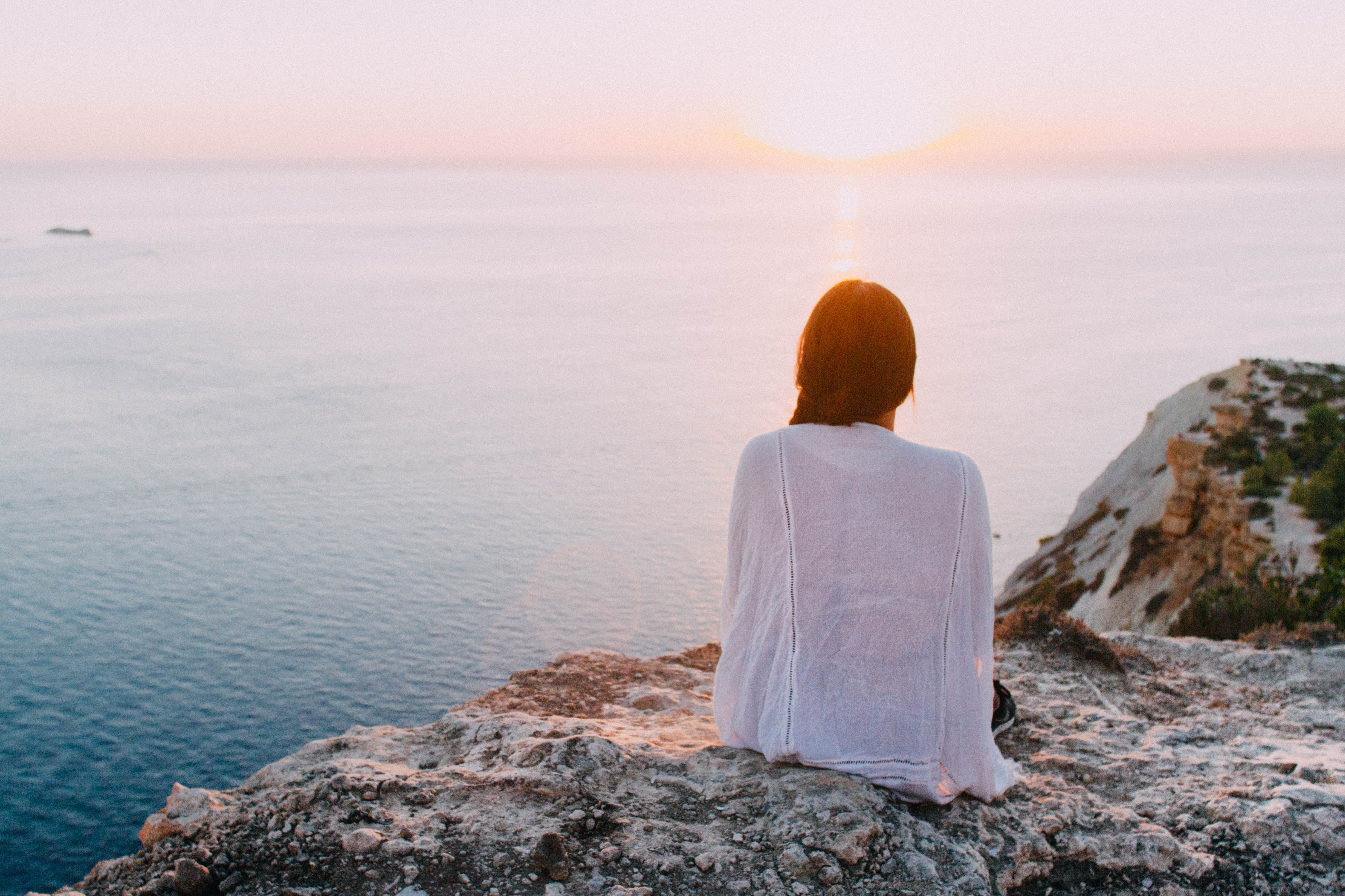 girl sitting on a rock facing the sunset, not getting results